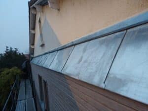 Installation de couverture en zinc sur une façade de maison avec un ouvrier sur un échafaudage.