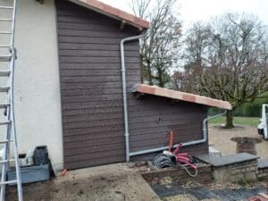 Façade avec bardage en bois marron, système de gouttière grise et toiture en tuiles lors de travaux de rénovation.