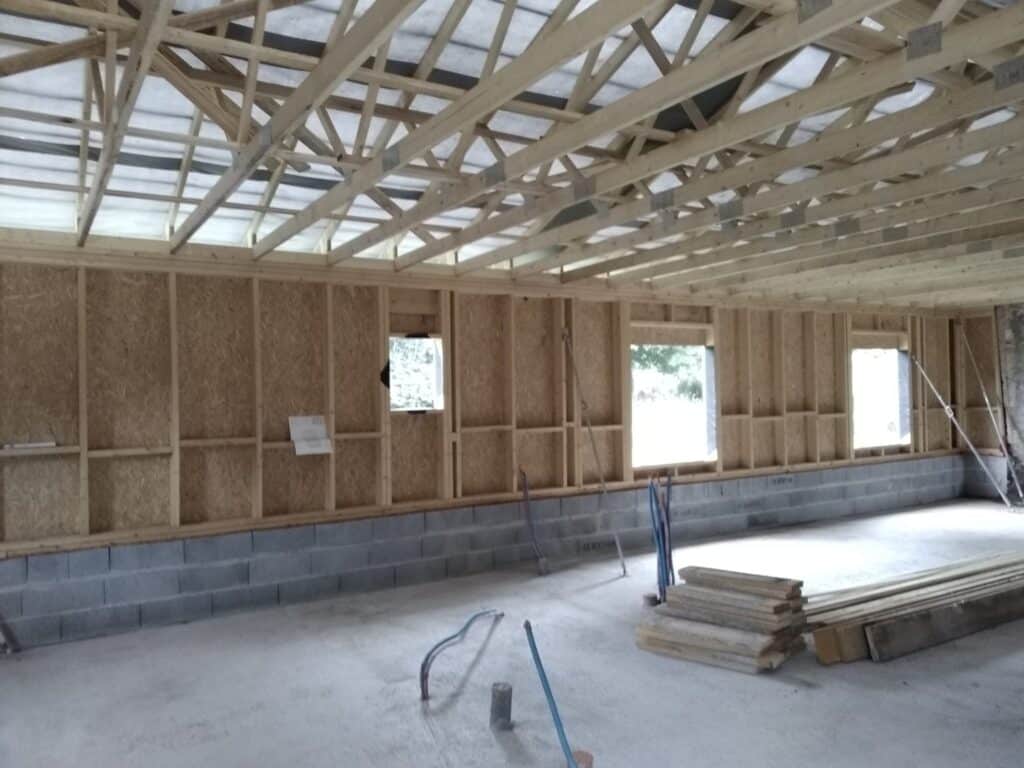 Maison à Ossature Bois : Charpente et Murs en Chantier Intérieur d'un bâtiment en construction avec charpente bois, murs en ossature et soubassement en parpaings.