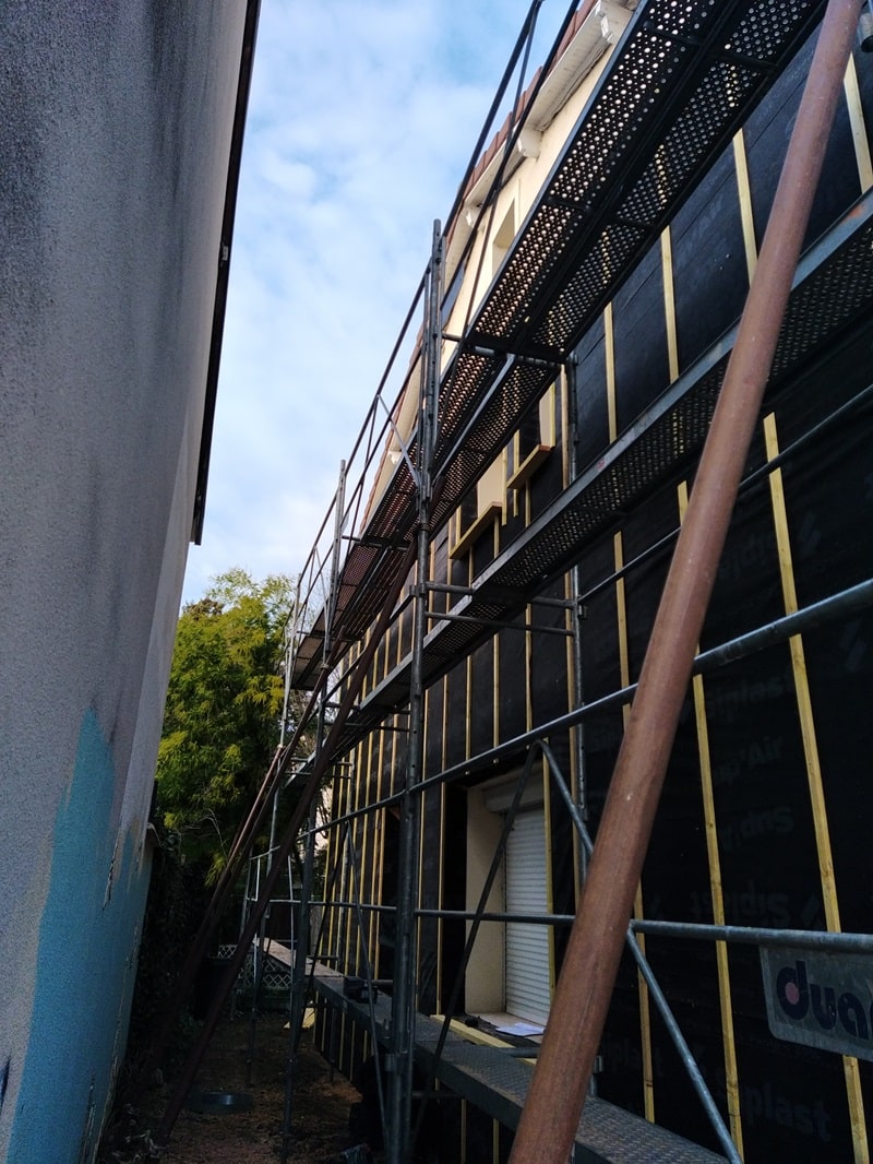 Échafaudage sur façade en rénovation avec membrane Siplast et tasseaux bois, travaux d'isolation extérieure en cours.
