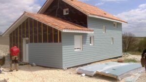 Ouvrier posant du bardage gris sur une façade avec membrane Delta Vent S et toit en tuiles orange.