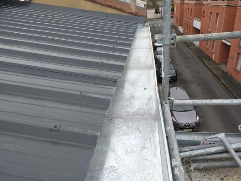 Toiture en bac acier gris avec gouttière en zinc et échafaudage lors d'une rénovation urbaine.
