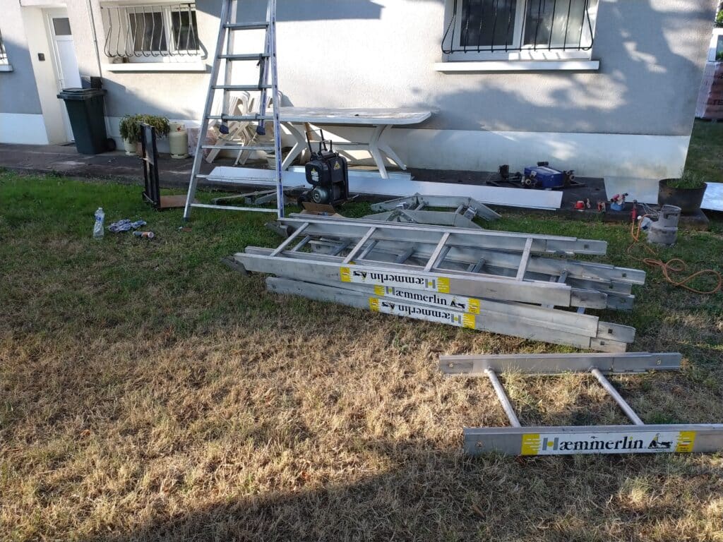 Échelles de chantier Hæmmerlin et matériel de travaux sur une pelouse devant une maison.