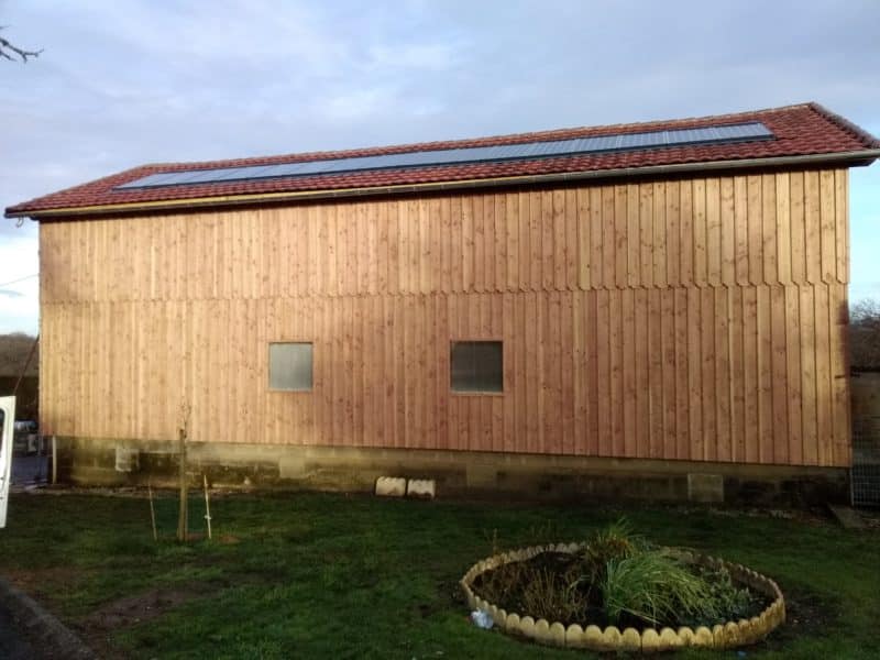 Grange en bois moderne avec panneaux solaires Grange en bois avec panneaux solaires sur toit de tuiles rouges dans un jardin verdoyant.