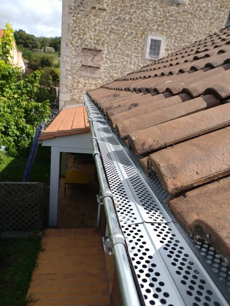 Pare-feuilles métallique perforé sur gouttière de toit en tuiles romaines, protection efficace contre les débris.